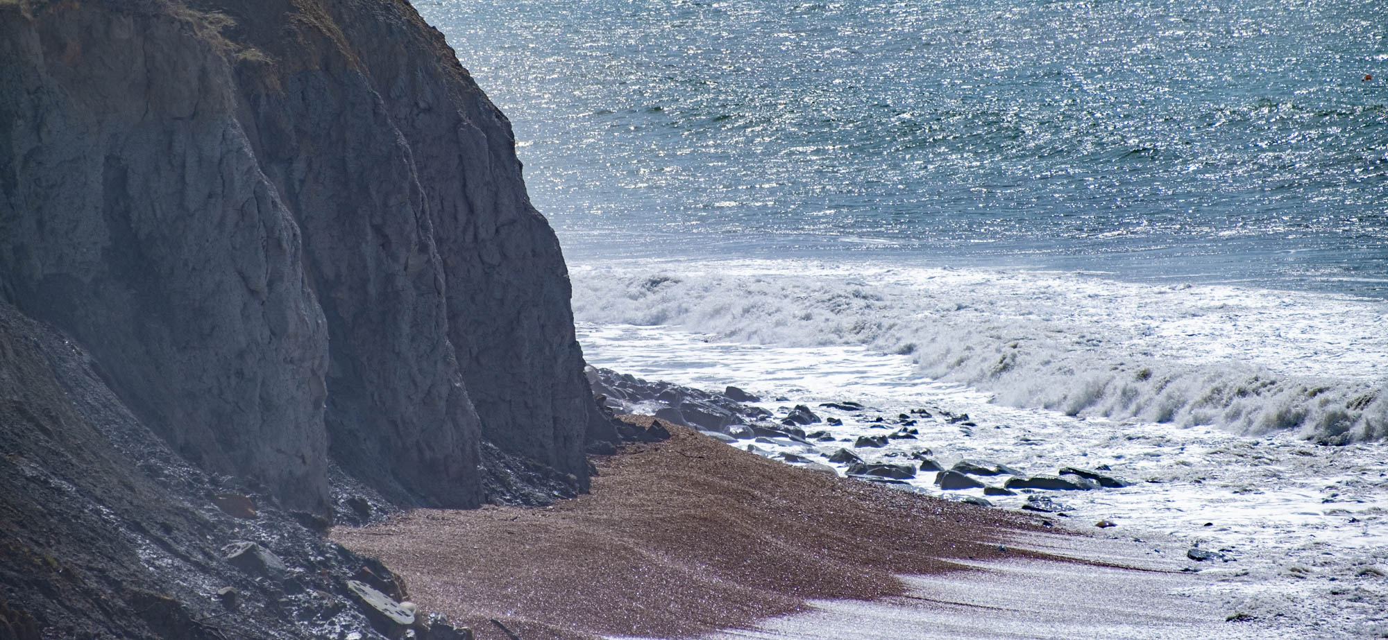breaking waves on a sandy beach, with steep cliffs behind